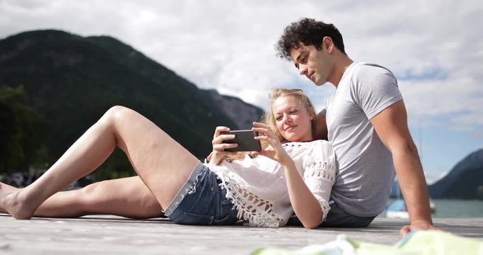 Couple relaxing on jetty looking at smartphone