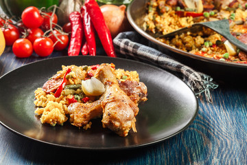 Traditional paella with chicken legs, sausage chorizo and vegetables served on black plate