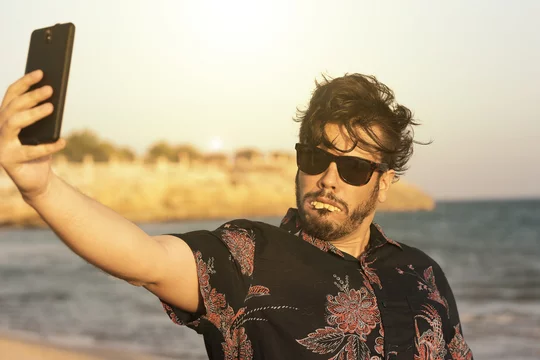 O homem feio usa camisa azul florida e oculos no dia ensolarado e quente na  praia. Homem engraçado fazendo selfie com o seu telefone celular smart.  Stock Photo | Adobe Stock