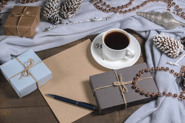 A cup of black coffee and gifts in a Christmas decor and a sheet of paper with a pen for text top view