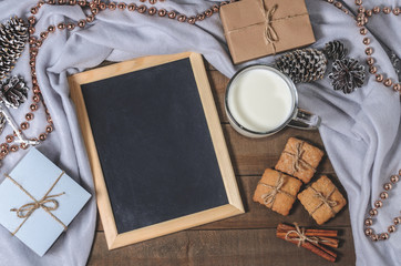 A cup of milk, cinnamon sticks, homemade biscuits and a slate in Christmas decor.