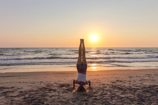 Frau macht Kopfstand am Strand im Sonnenuntergang