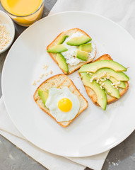 Breakfast. Eggs on toast with avocado, soft white cheese, spices and nuts. White plate, gray concrete background.