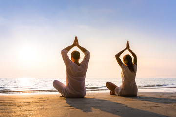 Couple practicing yoga on the beach in morning sunlight, relaxation