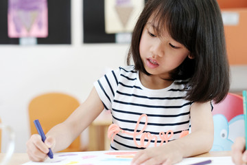 Asian girl drawing color pencils in kindergarten classroom, preschool and kid education concept