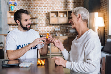 So useful. Kind cheerful young social worker recommending useful pills to a smiling senior man while visiting him