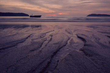 Sunset over Pantai Cenang beach with pink colours, blur background and silhouette of boat. Langkawi, Malaisiya.