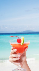 Strawberry Daiquiri cocktail in woman's hand at the beach restaurant over beautiful blue sea and sky background