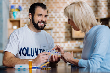 So easy. Cheerful curious pensioner trying to use a new convenient pill box while a happy volunteer helping her to do it