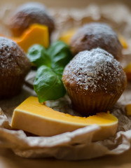 Tasty homemade muffins with powdered sugar decoration and 	pumpkin on the white plate on the wooden table