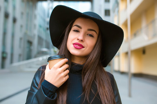 Lifestyle portrait of beautiful brunette model with cup of coffee wearing broad brimmed hat. Coffee to go concept