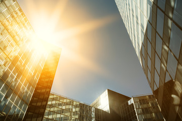 Skyscraper glass facades on a bright sunny day with sunbeams in the blue sky. Modern buildings in Paris business district La Defense. Economy, finances, business activity concept. Bottom up view
