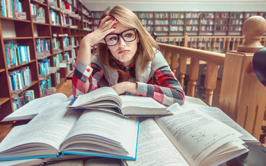 Confused and tired casual stylish student girl wears glasses studying hard with books in the...