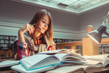 Successful casual stylish student girl wears glasses studying hard with books in the library,...