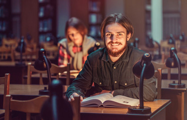 Portrait of two successful students casual stylish, boy and girl in library reading hall, evening time, education concept