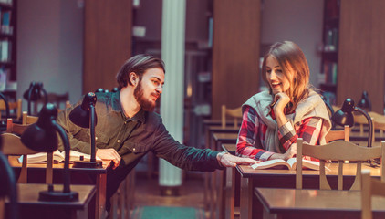 Portrait of two successful students casual stylish, boy and girl in library reading hall, evening time, education concept