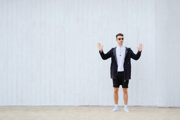 Fototapeta na wymiar fashionable man on a white wall stands on the sand. raises his hands up. left side for text