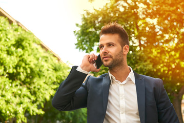 Young businessman talking on a phone on the sunny street