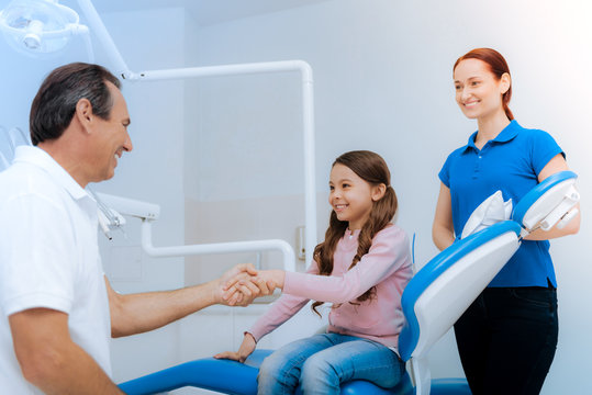 Nice To Meet You. Delighted Positive Young Girl Looking At Her Doctor And Smiling While Greeting Him