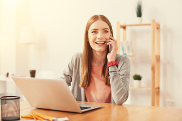 Obraz premium Exchanging news. Positive smiling young student looking happy while talking to her friend and sitting with a laptop in a local reading room