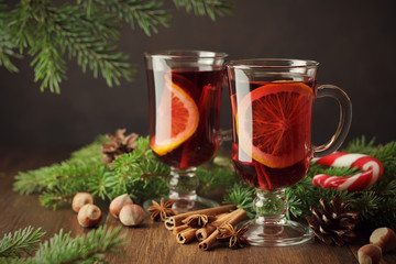 Christmas mulled wine in glasses with orange slice on rustic wooden background with pine branches, spices, nuts.