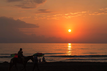 Fototapeta na wymiar Peaceful walk along a beach. Sunny evening beach walk. The silhouettes people at the sunset background