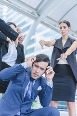 Colleagues business team pointing thumbs down bad negative gesture to business man while project failed in cityscape background