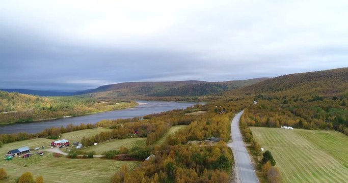 Autumn color landscape, Cinema 4k aerial decreasing view of mountains and countryside fields, full of different fall colors, near tenojoki river, on a cloudy day, in Lapland, Finland