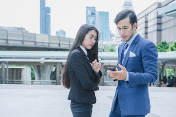 Fototapeta premium Profession businessman and businesswoman using smartphone for work outside office in cityscape background