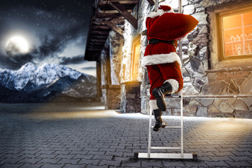The old Santa Claus in a red costume walks up the silver ladder. Old house in the mountains with many windows and orange light. Landscape of winter mountains with huge moon in the sky.