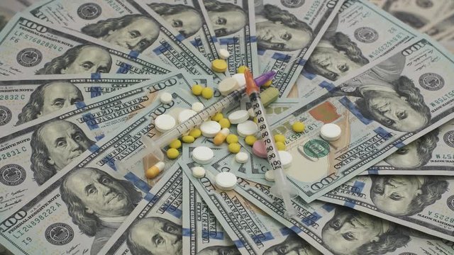 Heap of mixed pills and syringes rotating on money - healthcare cost concept