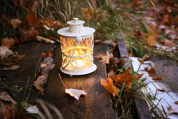 Decorative lantern with burning candle in autumn park at evening.