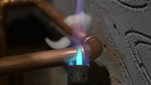Plumber uses blow torch to braze solder on copper water pipe elbow fittings England May 2017