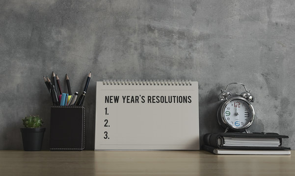 New Year Resolutions, Notes, Goals, Post, Memo Or Action Plan Concept. Calendar With Blank Space For Input Text With Clock, Notebook, Plant And Stationery On Wooden Desk, Loft Wall At Home Or Office.