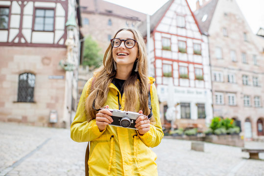 Young woman tourist in yellow raincoat standing with backpack on the old square with beautiful buildings on the background in Nurnberg city, Germany