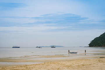 Fototapeta na wymiar Tourist walking on the beach with fishing boat in the background.