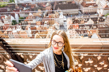 Young woman tourist making selfie photo standing on the terrace with great aerial view on the old town in Strasbourg city, France