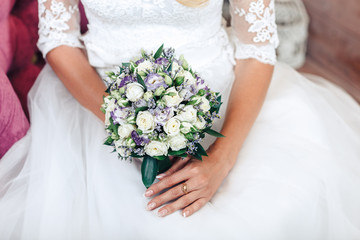 wedding bouquet of white and purple roses in the hands of brides, close-up, on a white dress background
