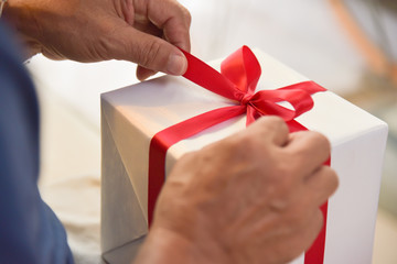 Asian elderly man holding on red ribbon of white gift box.