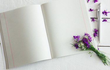 open a clean notebook on a wooden white table with flowers and petals
