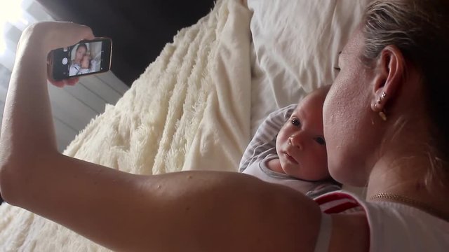 Mother and newborn baby doing selfie on bed. Resting in bed together. Maternity concept. Parenthood. Motherhood Beautiful Happy Family Stock Video Footage.