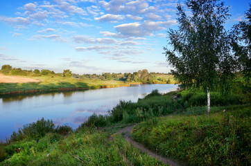 Sunny summer landscape.Morning calm.Scene with ground countryside road and birch.River Krasivaya in Tula region,Russia. 