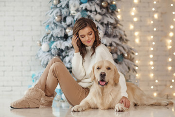 Beautiful young woman with a golden retriver dog near christmas tree