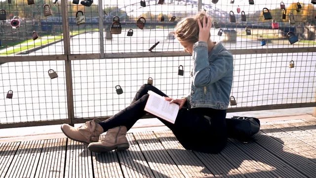 Young, pretty woman reading book sitting on the bridge in the city
