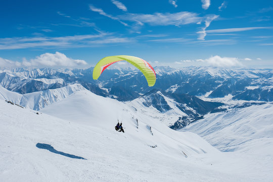 Paraglider flying between the jagged snowy peaks
