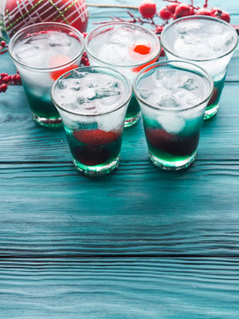 Christmas holiday party background with green alcohol drinks with cherry. Festive aperitif shots and ornaments on wooden dark table