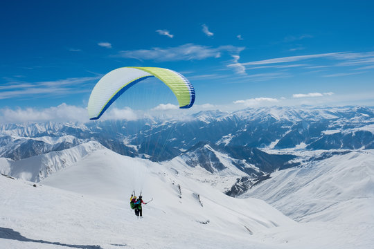 An athlete with a passenger on a paraglider flying over snowy mountains