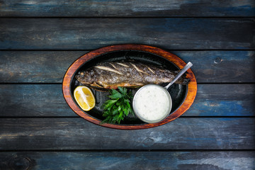 Obraz na płótnie Canvas Frying pan with tasty trout fish on wooden background wine greens, sauce and lemon