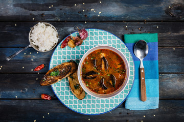 Seafood tomato soup with bread and rice for a garnish on a colored wooden background. Top view