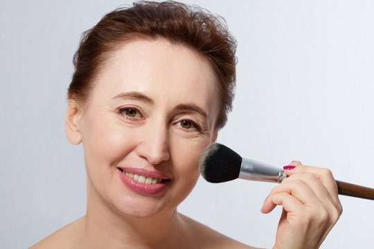 Beautiful senior, middle age, mature woman applying make up by make-up brush isolateds. Macro and close-up Face with wrinkles. Mock up and copy space.